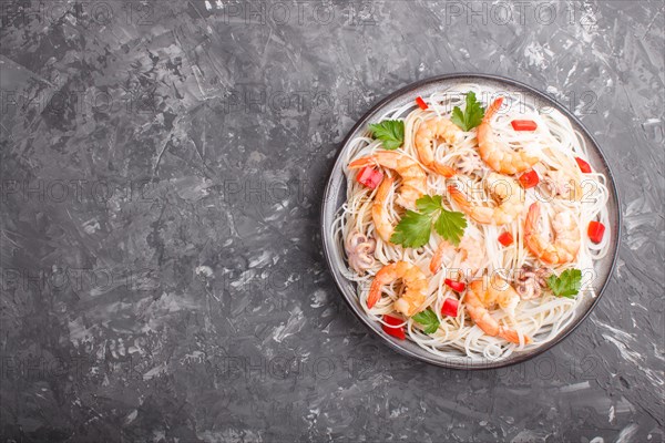 Rice noodles with shrimps or prawns and small octopuses on gray ceramic plate on a black concrete background. Top view, flat lay, copy space