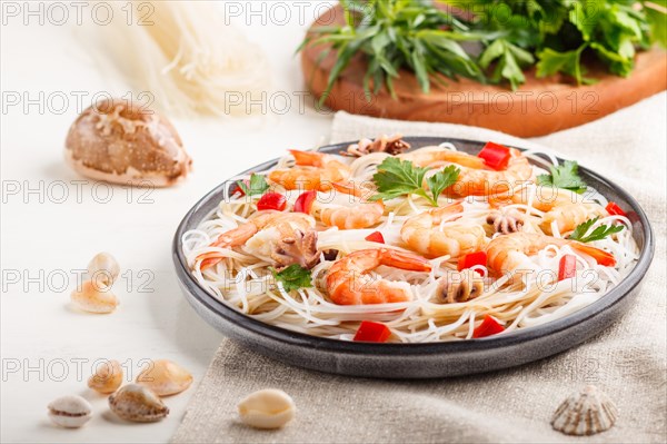 Rice noodles with shrimps or prawns and small octopuses on gray ceramic plate on a white wooden background and linen textile. side view, close up, selective focus