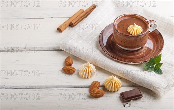 Cup of hot chocolate and pieces of milk chocolate with almonds on a white wooden background with linen napkin. side view, copy space