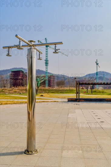 Chrome public shower sprinklers in empty rural park with construction cranes in background in South Korea