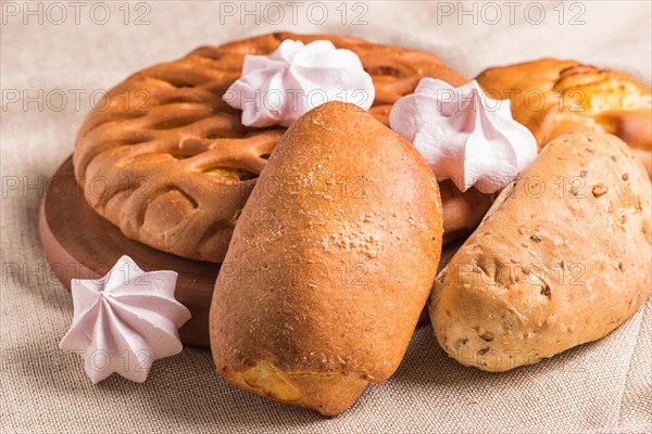 Sweet buns and meringues on a wooden board and linen tablecloth