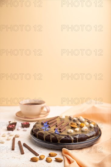 Homemade chocolate brownie cake with caramel cream and almonds with cup of coffee on a white and orange background and orange textile. Side view, copy space, selective focus
