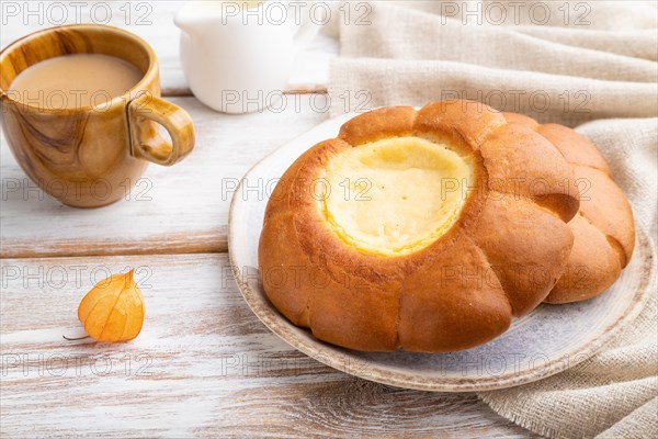 Sour cream bun with cup of coffee on a white wooden background and linen textile. Side view, close up