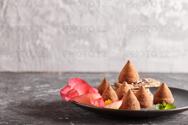 Chocolate truffle on blue ceramic plate decorated with rose petals on black concrete background. close up, side view. copy space