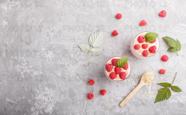 Yoghurt with raspberry and sesame in a glass and wooden spoon on gray concrete background. top view, flat lay, copy space
