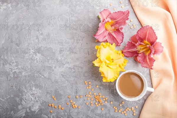 Yellow anf purple day-lilies cup of coffee on a gray concrete background, with orange textile. Morninig, spring, fashion composition. Flat lay, top view, copy space