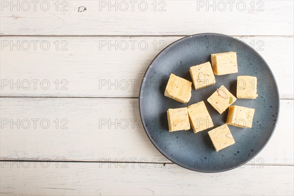 Traditional indian candy soan papdi in a blue ceramic plate with almond and pistache on a white wooden background. top view, flat lay, copy space