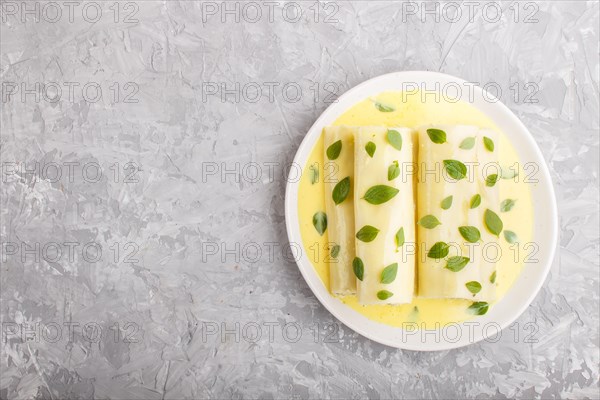 Cannelloni pasta with egg sauce, cream cheese and oregano leaves on a gray concrete background. top view, flat lay, copy space