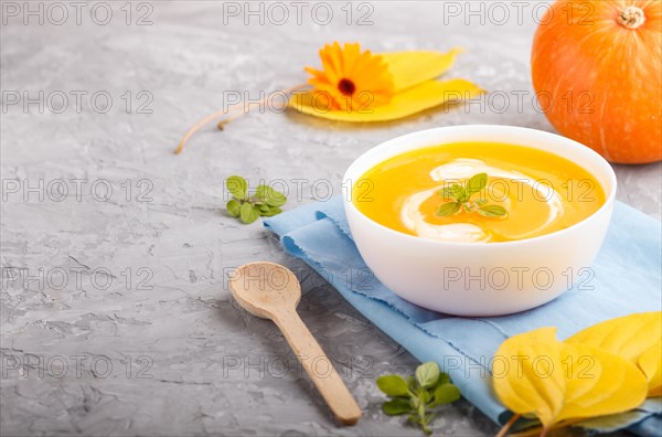 Traditional pumpkin cream soup with in white bowl on a gray concrete background with blue napkin. side view, close up, selective focus, copy space