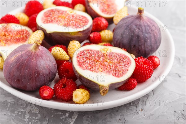 Fresh figs, strawberries and raspberries on white ceramic plate on gray concrete background. side view, close up, selective focus