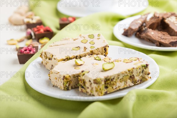 Traditional arabic sweets sesame halva with chocolate and pistachio and a cup of coffee on green textile background. side view, close up, selective focus