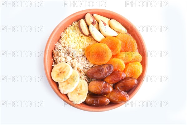 A plate with muesli, banana, dried apricots, dates, Brazil nuts isolated on a white background. top view