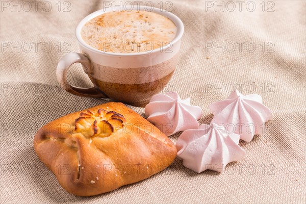 Sweet buns, meringues and coffee cup on a wooden board and linen tablecloth