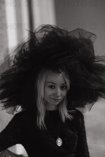 A black and white portrait captures the textured mystery of a blonde caucasian young woman's oversized hat veil