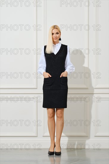 Cute woman in school uniform with hands in pockets next to white wall