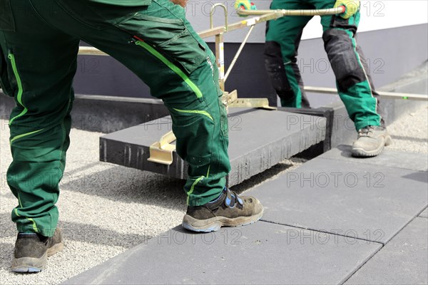 Workers lay heavy paving stones with a stone lifter
