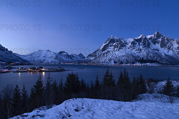 Blick auf verschneite Berge und einen Fjord in Norwegen waehrend der blauen Stunde, Lofoten