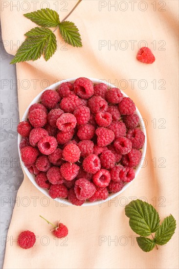 Fresh raspberry in white bowl and orange pastel textile on gray concrete background. top view, flat lay, close up