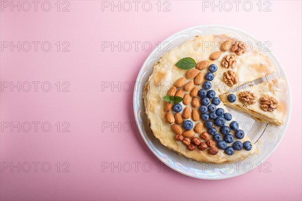 Homemade layered Napoleon cake with milk cream. Decorated with blueberry, almonds, walnuts, hazelnuts, mint on a pastel pink background. top view. flat lay, copy space