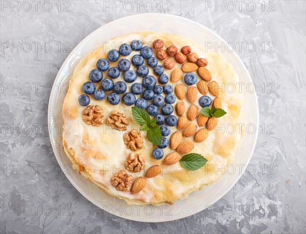 Homemade layered Napoleon cake with milk cream. Decorated with blueberry, almonds, walnuts, hazelnuts, mint on a gray concrete background. top view. flat lay, close up