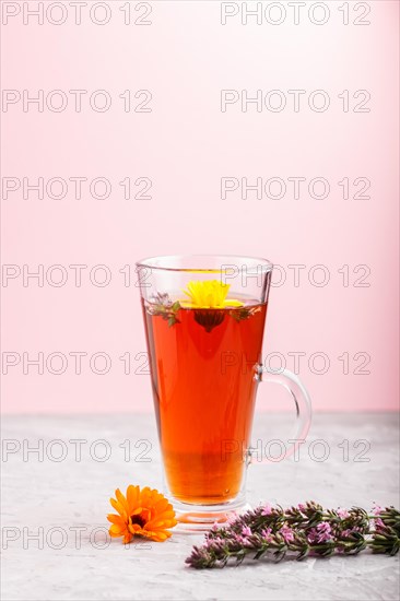 Glass of herbal tea with calendula and hyssop on a gray and pink background. Morninig, spring, healthy drink concept. Side view, selective focus, copy space