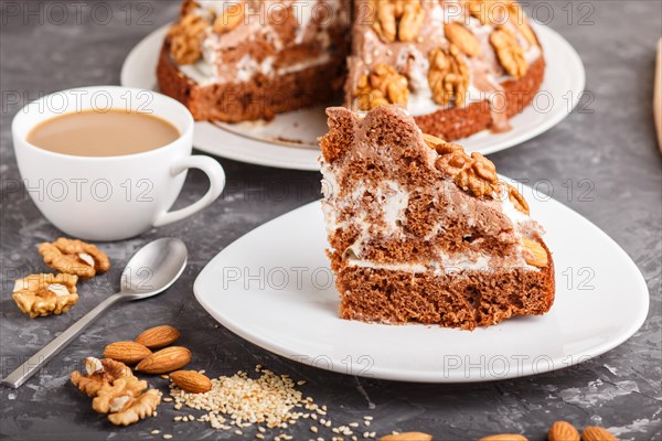 Homemade cake with milk cream, cocoa, almond, hazelnut on a black concrete background and a cup of coffee. Side view, close up, selective focus