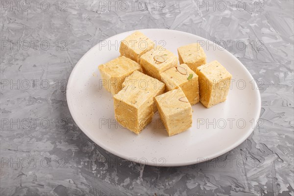 Traditional indian candy soan papdi in white plate with almond and pistache on a gray concrete background. side view, close up