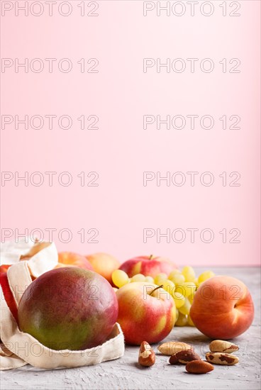 Fruits in reusable cotton textile white bag. Zero waste shopping, storage and recycling concept, eco friendly lifestyle. Side view, close up, copy space. Peach, apple, nuts, mango, grape