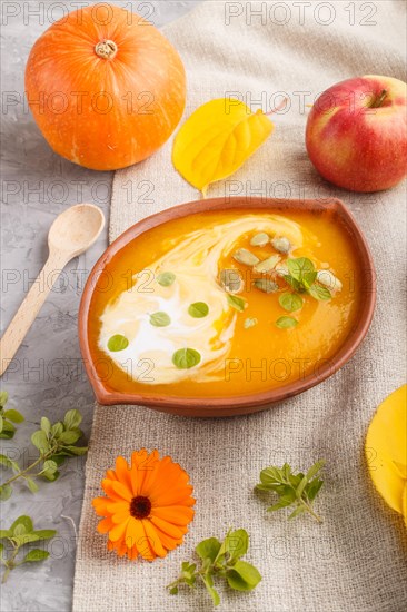 Traditional pumpkin cream soup with seeds in clay bowl on a gray concrete background with linen textile. side view, close up