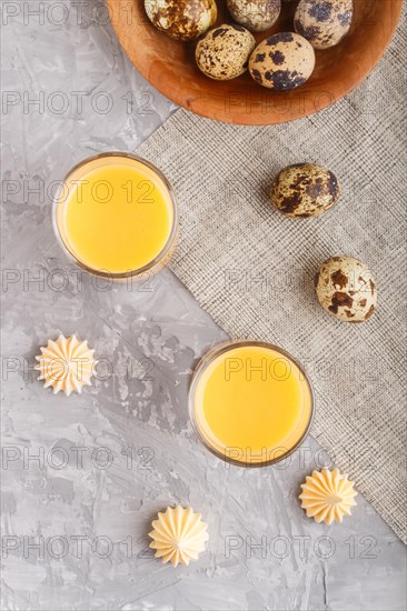 Sweet egg liqueur in glass with quail eggs and meringues on a gray concrete background. Top view, close up, flat lay