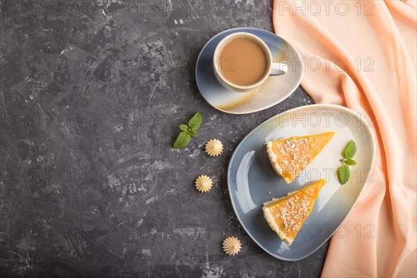 Two pieces of traditional american pumpkin pie with cup of coffee on a black concrete background and orange textile. top view, flat lay, copy space, contrast