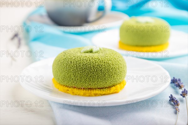 Green mousse cake with pistachio cream and a cup of coffee on a white wooden background and blue textile. side view, close up, selective focus