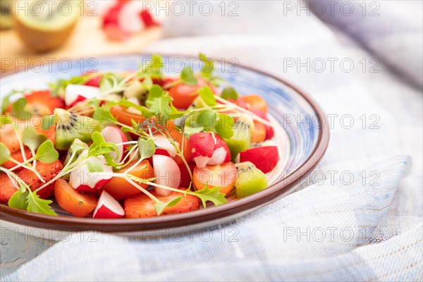 Vegetarian fruits and vegetables salad of strawberry, kiwi, tomatoes, microgreen sprouts on white concrete background and linen textile. Side view, close up, selective focus