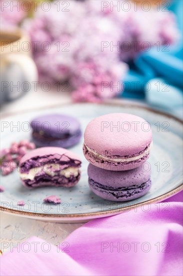 Purple macarons or macaroons cakes with cup of coffee on a white concrete background and magenta-blue textile. Side view, close up, selective focus