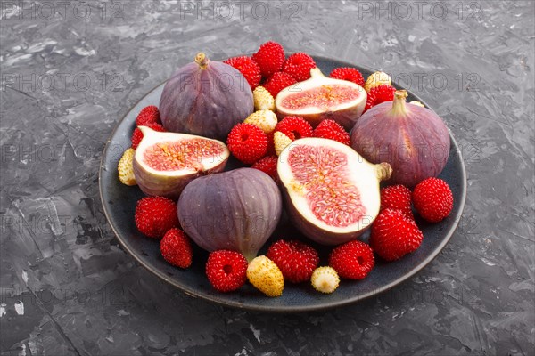 Fresh figs, strawberries and raspberries on blue ceramic plate on black concrete background. side view, close up