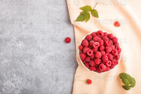 Fresh raspberry in white bowl and orange pastel textile on gray concrete background. top view, flat lay, copy space