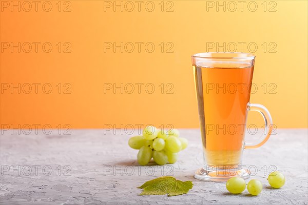 Glass of green grape juice on a gray and orange background. Morninig, spring, healthy drink concept. Side view, copy space