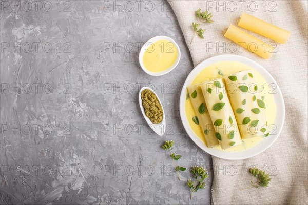 Cannelloni pasta with egg sauce, cream cheese and oregano leaves on a gray concrete background with linen textile. top view, flat lay, copy space