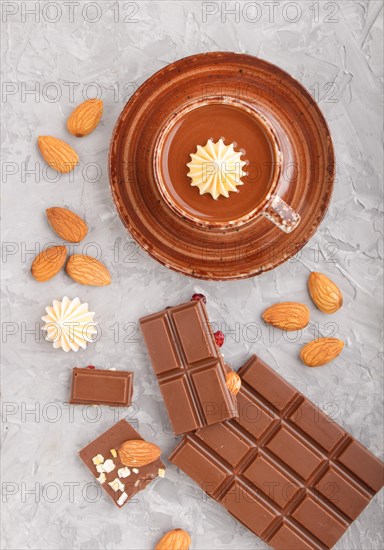 Cup of hot chocolate and pieces of milk chocolate with almonds on a gray concrete background. Flat lay, top view, close up