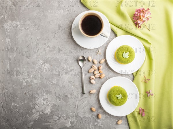 Green mousse cake with pistachio cream and a cup of coffee on a gray concrete background and green textile. top view, flat lay, copy space