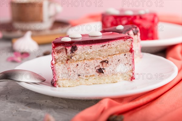 Sliced red cake with souffle cream with cup of coffee on a gray concrete background and red textile. side view, close up. selective focus