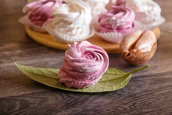 Pink and white homemade marshmallows (zephyr) on a round wooden board with seashells on a gray wooden background