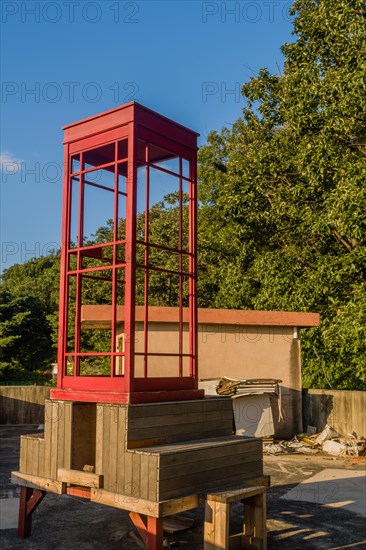 Red wooden telephone booth minus phone and without glass on roof of building on sunny day with blue skies in South Korea