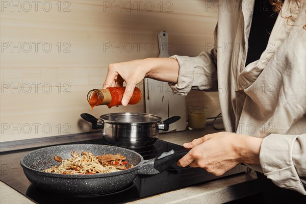 Unrecognizable woman pouring sweet chilli sauce into noodles in a frying pan