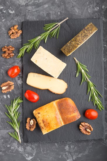Smoked cheese and various types of cheese with rosemary and tomatoes on black slate board on a black concrete background. Top view, close up, flat lay
