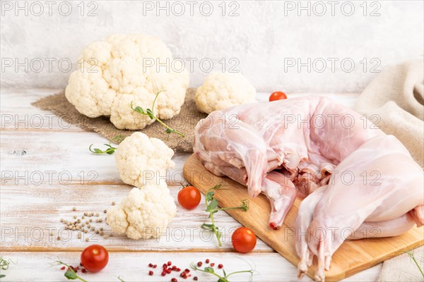 Whole raw rabbit with cauliflower, tomatoes and spices on a white wooden background and linen textile. Side view, close up, selective focus