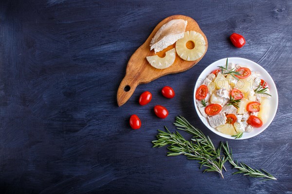 Chicken fillet salad with rosemary, pineapple and cherry tomatoes on dark blue wooden background. top view, copy space