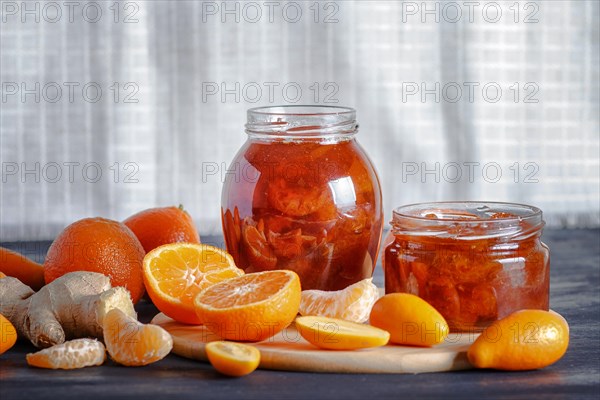 Tangerine and kumquat jam in a glass jar with fresh fruits on a black wooden table and white linen background. Homemade, copy space