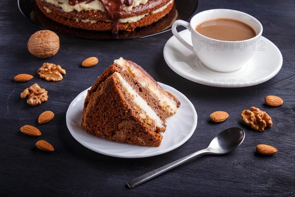 Homemade chocolate cake with milk cream, caramel and almonds on black wooden background. cup of coffee, close up