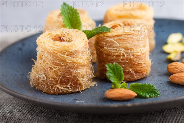 Kunafa, traditional arabic sweets in blue ceramic plate on a gray concrete background. side view, close up, selective focus